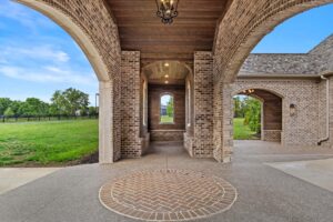 A circular brick driveway pattern underneath a covered motor-court clad in ranchwood Eastern cedar siding.