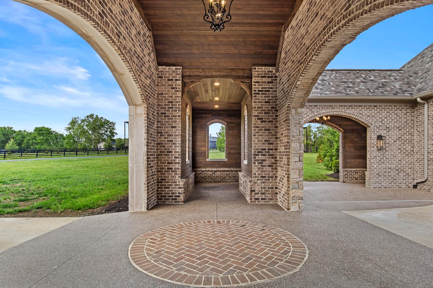 A circular brick driveway pattern underneath a covered motor-court clad in ranchwood Eastern cedar siding.