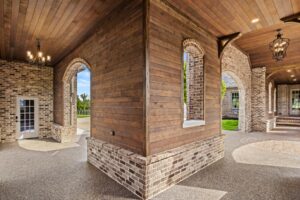 A covered breezeway with a wood ceiling and brick arches framed by smooth ranchwood Eastern cedar siding.