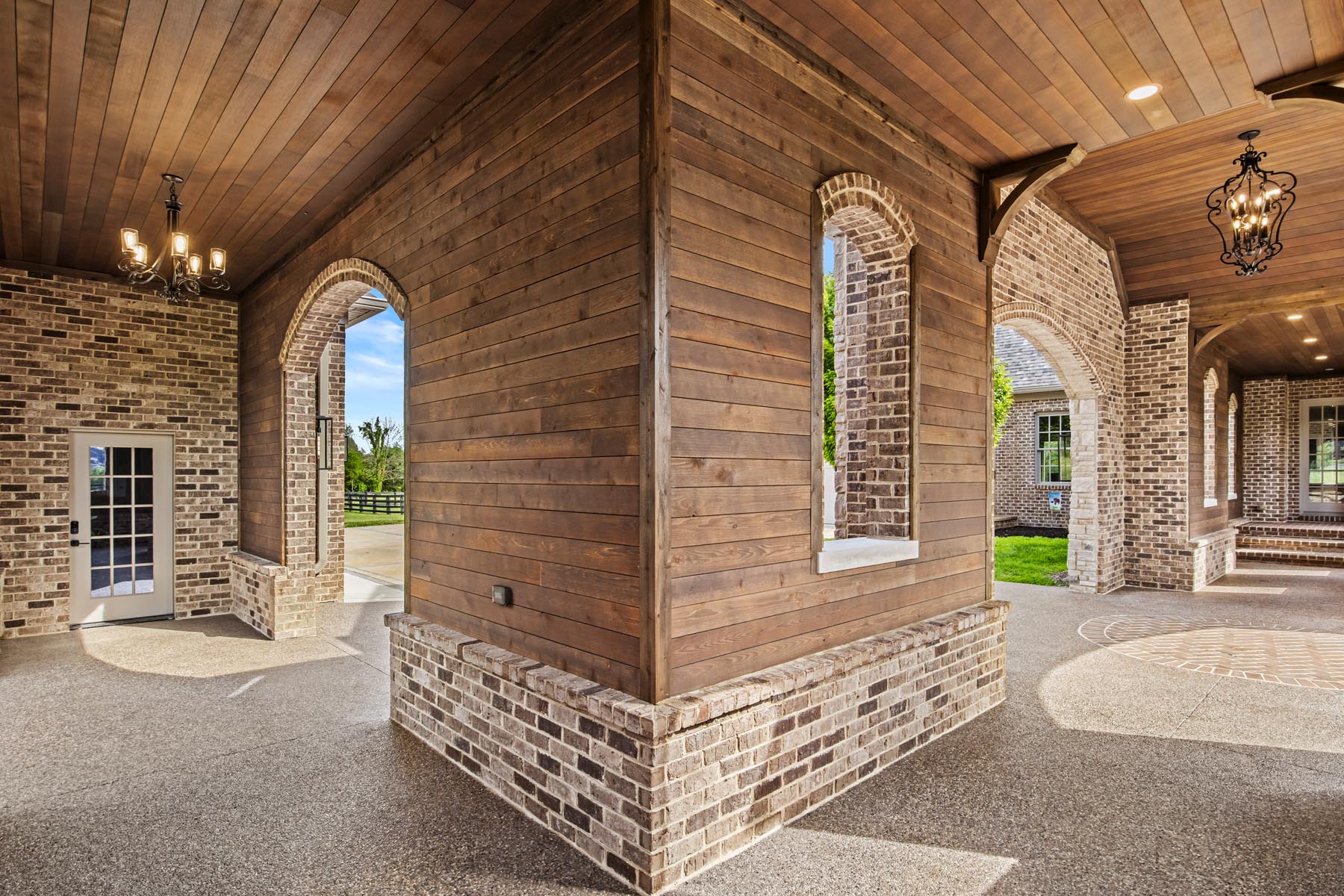 A covered breezeway with a wood ceiling and brick arches framed by smooth ranchwood Eastern cedar siding.
