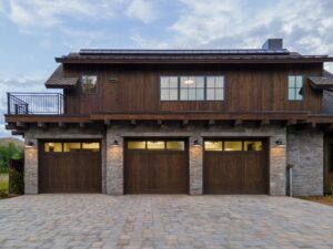 Exterior view of a luxury three-car garage featuring vertical ranchwood Western Douglas Fir shiplap siding and traditional stone masonry.