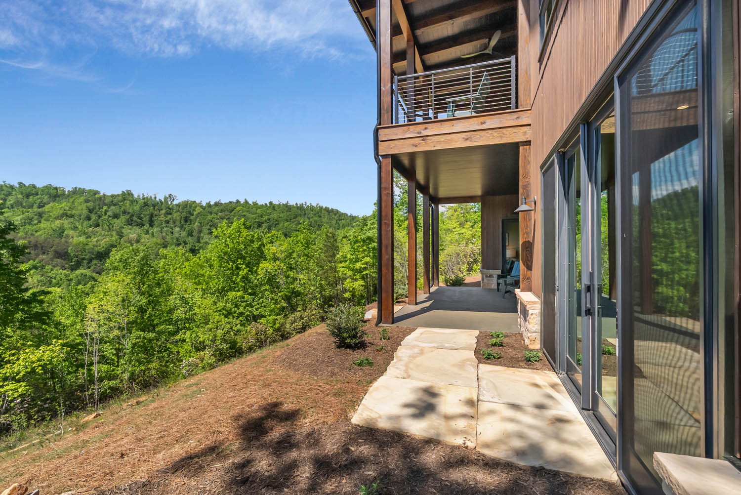 Covered back patio and upper balcony showing vertical thermally modified Southern Yellow Pine wood siding on a hillside elevation.