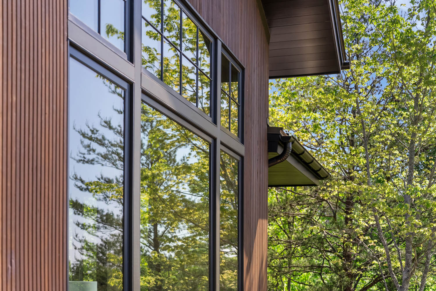 Close-up of custom triple-fluted Southern Yellow Pine wood siding adjacent to black window frames reflecting trees.