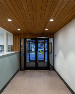 Close-up of interior entry door at Polson Public Library showing vertical wood wall siding lining up board-for-board with horizontal ceiling panels.